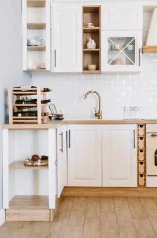 Modern kitchen design featuring white cabinets, wooden and stone countertops, a gold faucet, wine rack, open shelving, and a white subway tile backsplash.