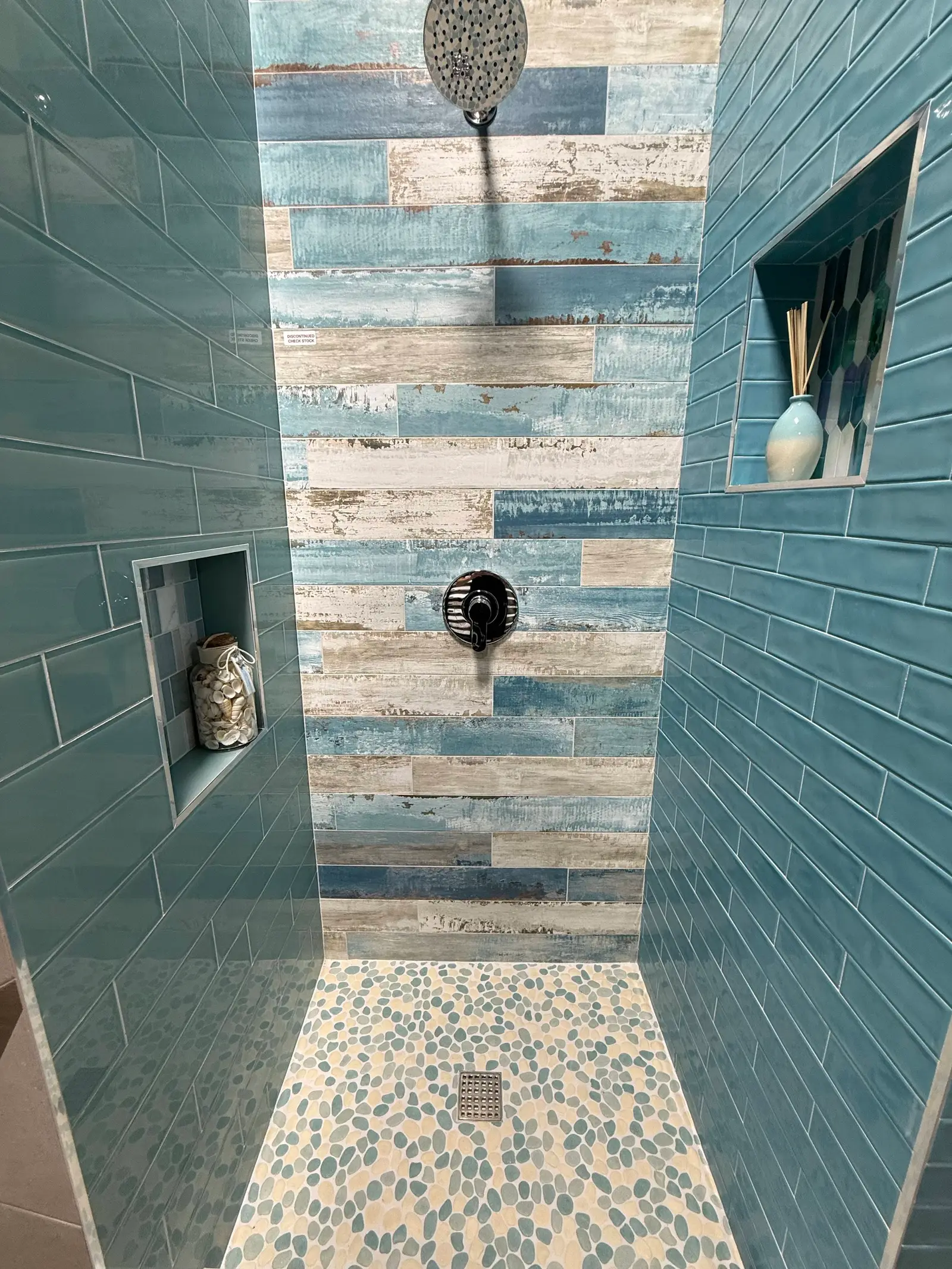 Shower with blue plank-look wall tile, recessed niches and a pebble floor
