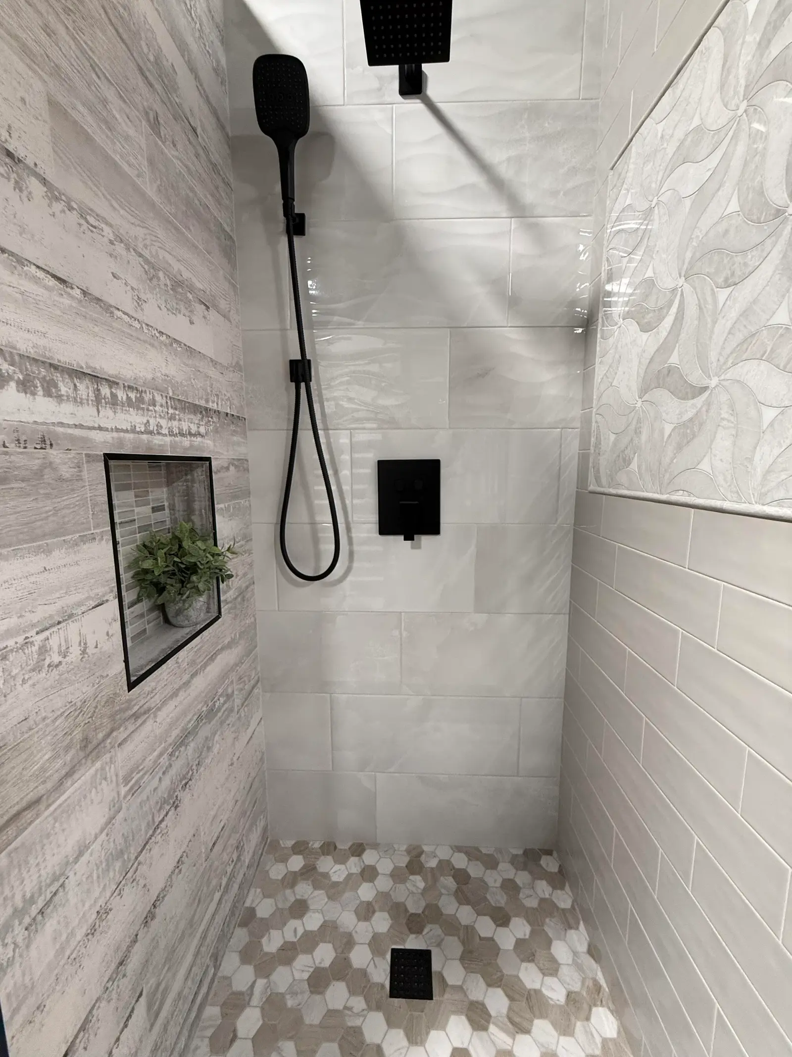 Shower with marble-look wall tile, matte black fixtures and a hex mosaic floor