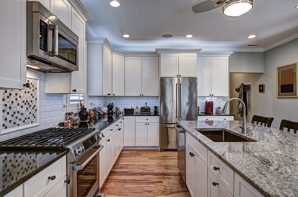 Modern kitchen with white cabinets, stainless steel appliances, granite countertops by J&A Stone Design, and a central island with a sink.