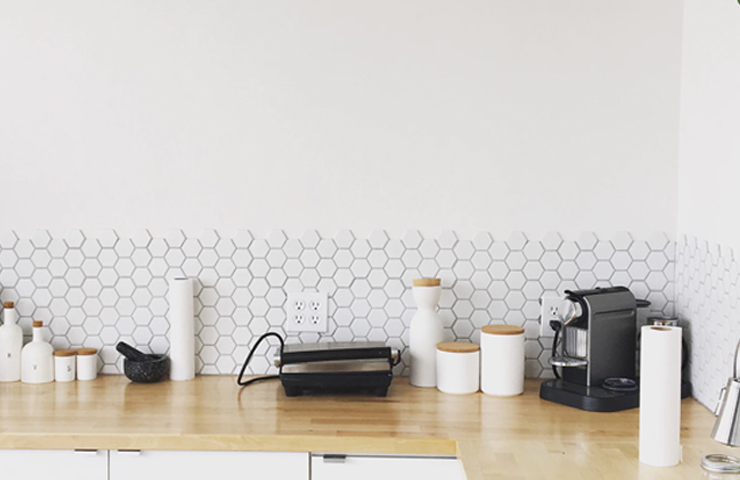 Kitchen counter with a hexagonal tile backsplash, wooden topped canisters, a panini press, and a coffee maker.