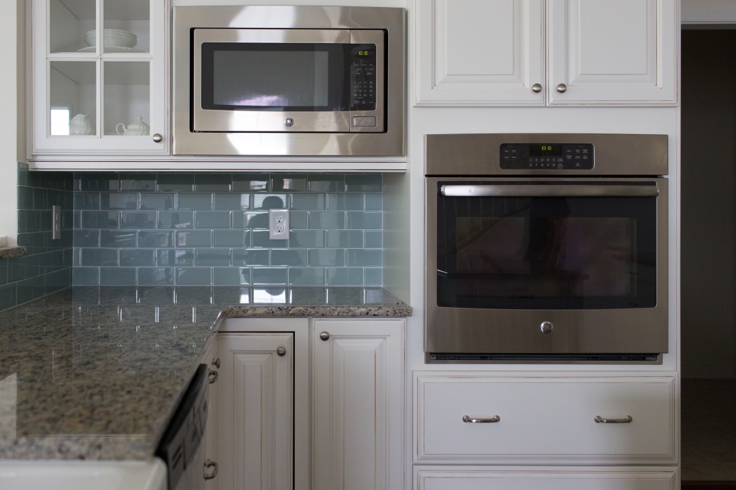 Modern kitchen with stainless steel microwave and oven, light blue tile backsplash, and expert granite countertop installation in Lakeland.