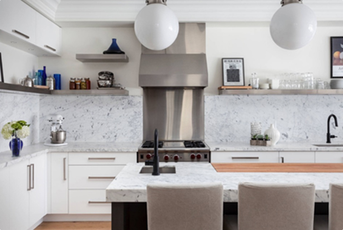 Modern kitchen with marble countertops, stainless steel appliances, and globe pendant lights. White cabinets contrast with a wooden island countertop and a black faucet.