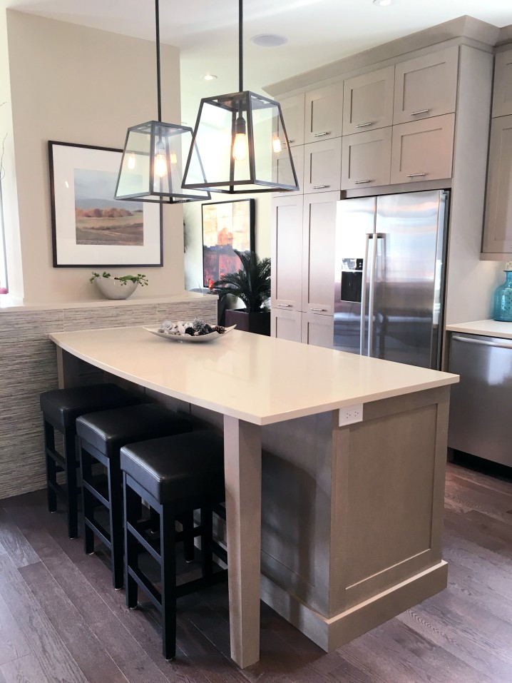 Experience a modern kitchen with a large island featuring quartz countertops, three bar stools, stainless steel appliances, pendant lights, and neutral cabinetry. Perfectly crafted for everyday elegance.