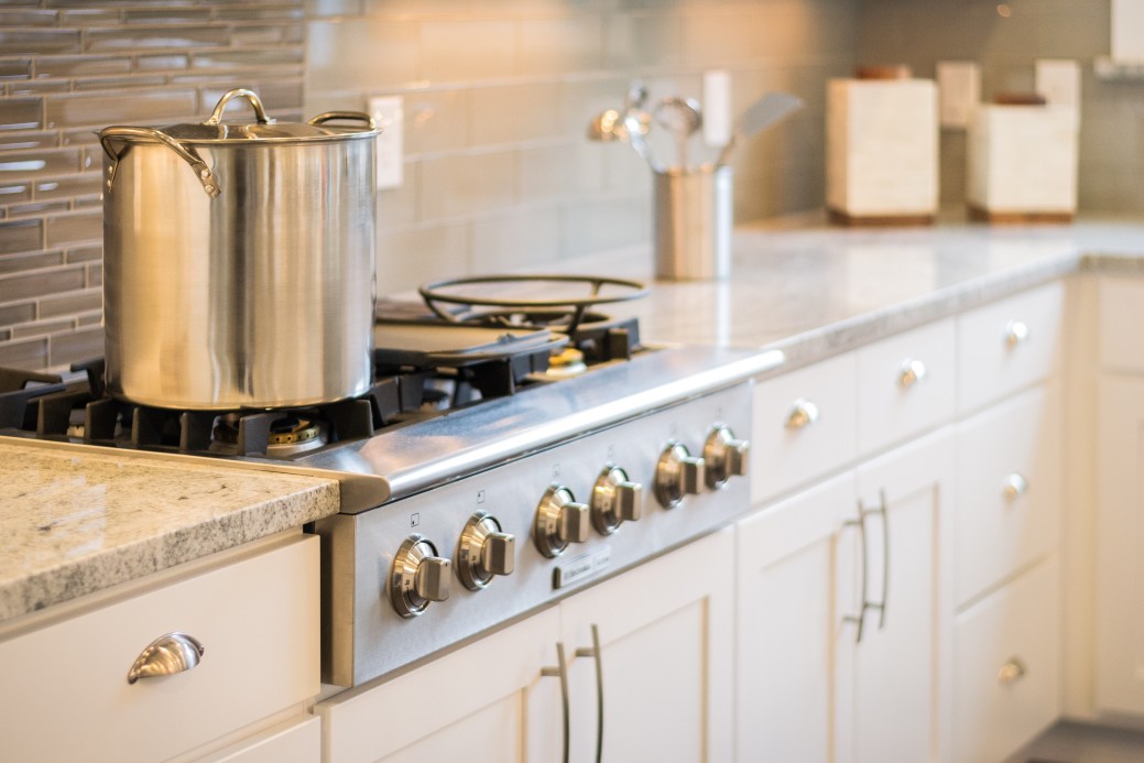 A stainless steel pot simmers on the stove in a modern kitchen, where sleek white cabinets contrast beautifully with a tiled backsplash and the recent marble countertop installation adds a touch of elegance.