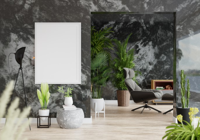 Modern luxury interior with a marble-patterned stone accent wall, potted plants, a blank framed picture, a black floor lamp, and a lounge chair near a bookcase.