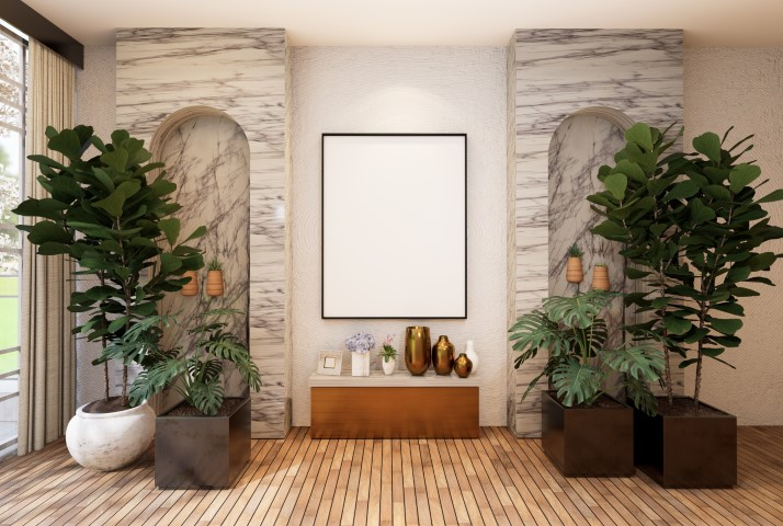Modern interior space with two large potted plants flanking a marble-accented stone accent wall, a wooden bench, decorative vases, and a blank square frame in the center for a touch of modern luxury.