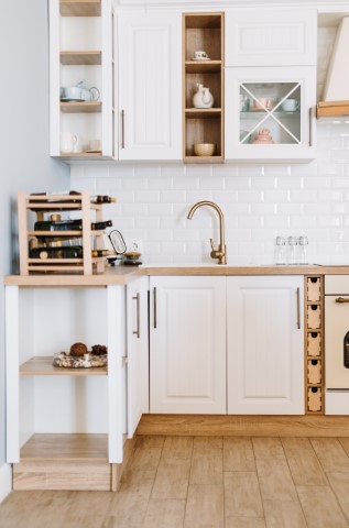 Modern kitchen design with white cabinets, stone countertops, a wine rack, ceramic dishes, and a stainless steel faucet, set against a white subway tile backsplash and light wooden floor.
