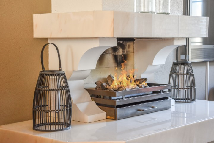 A modern fireplace with a lit fire, flanked by two black decorative lanterns on a white quartz fireplace surround.